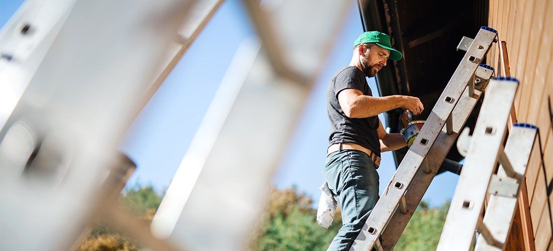 Side view of professional painter on ladder painting the side of a house.