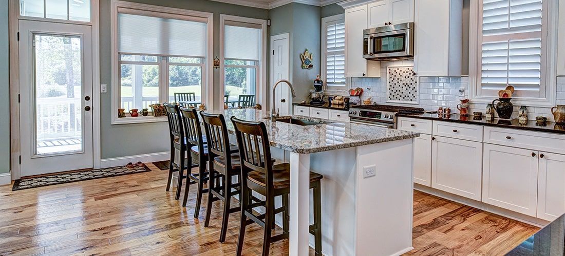 Modern kitchen with laminate flooring, white cupboards and island.