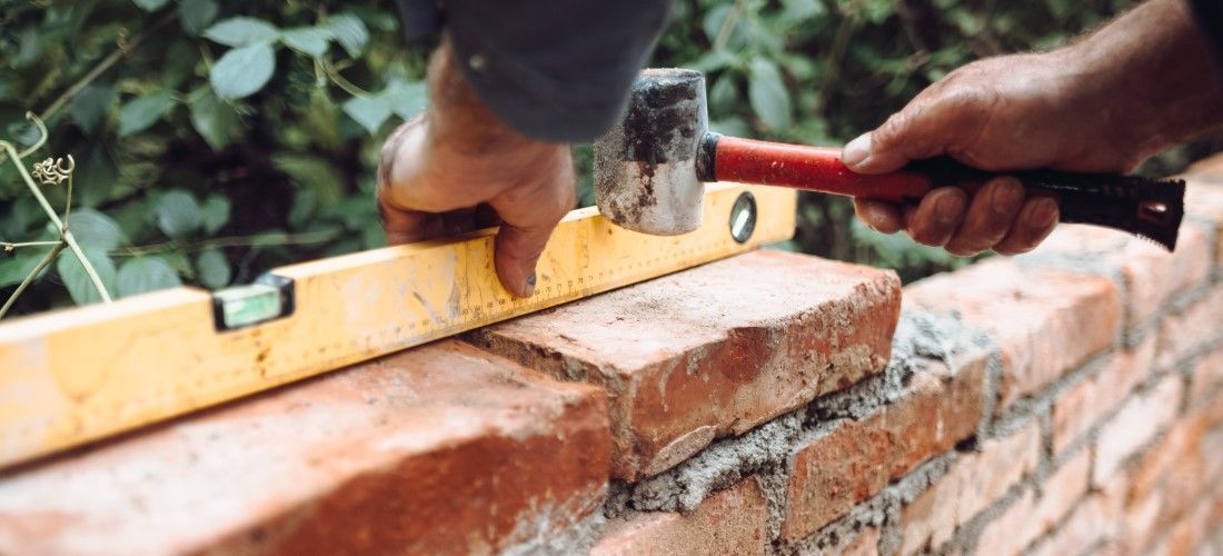 Worker tapping bricks into mortar with a club hammer to build a brick wall.