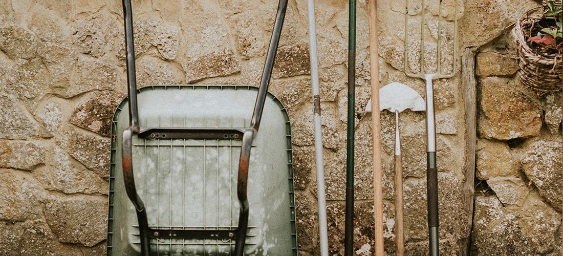 Garden tools leaning against stone wall.