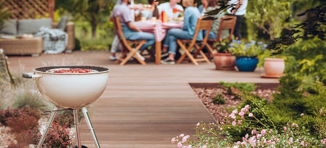 Grill on garden decking with bright summer flowers.