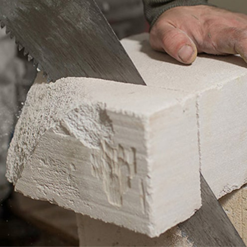 Man sawing block of foam with a panel saw.