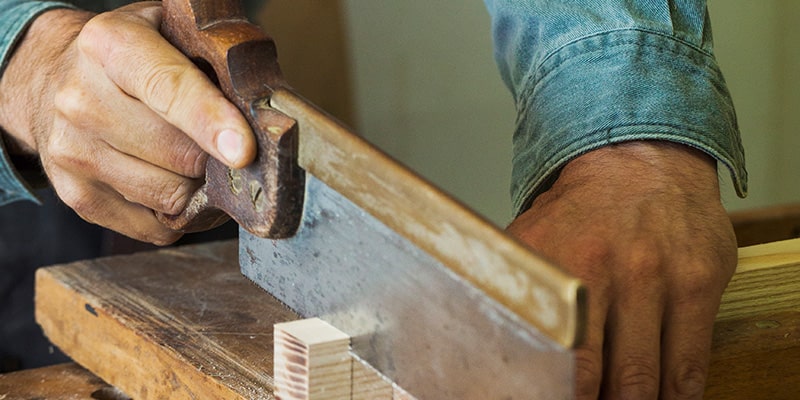 Wood worker cutting wooden block with a tenon saw.