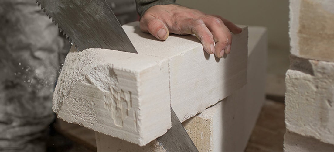 Man sawing block of foam with a panel saw.