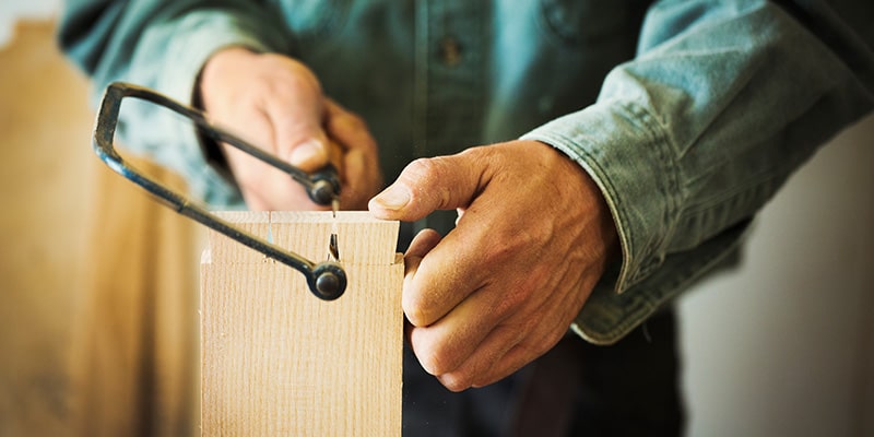 Wood worker cutting an angle out of a wooden block with a coping saw.