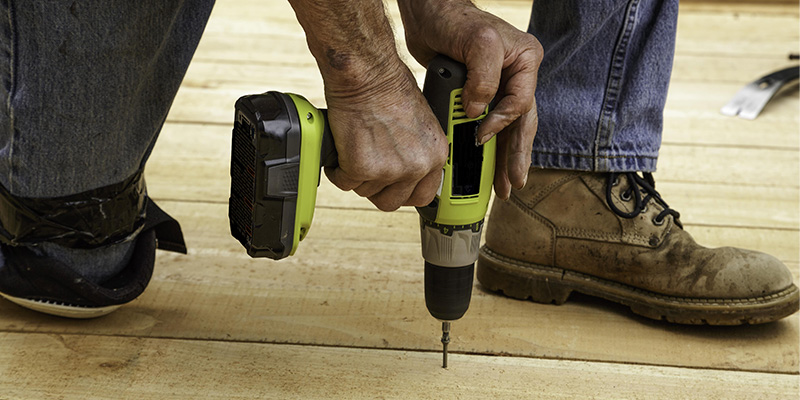 Handyman using cordless drill driver to install wooden flooring.