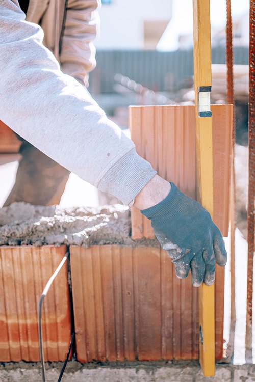 Builder measuring bricks with a lever whilst building a brick wall.