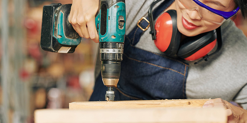 Carpenter using combi drill to drill a hole in a wooden block.