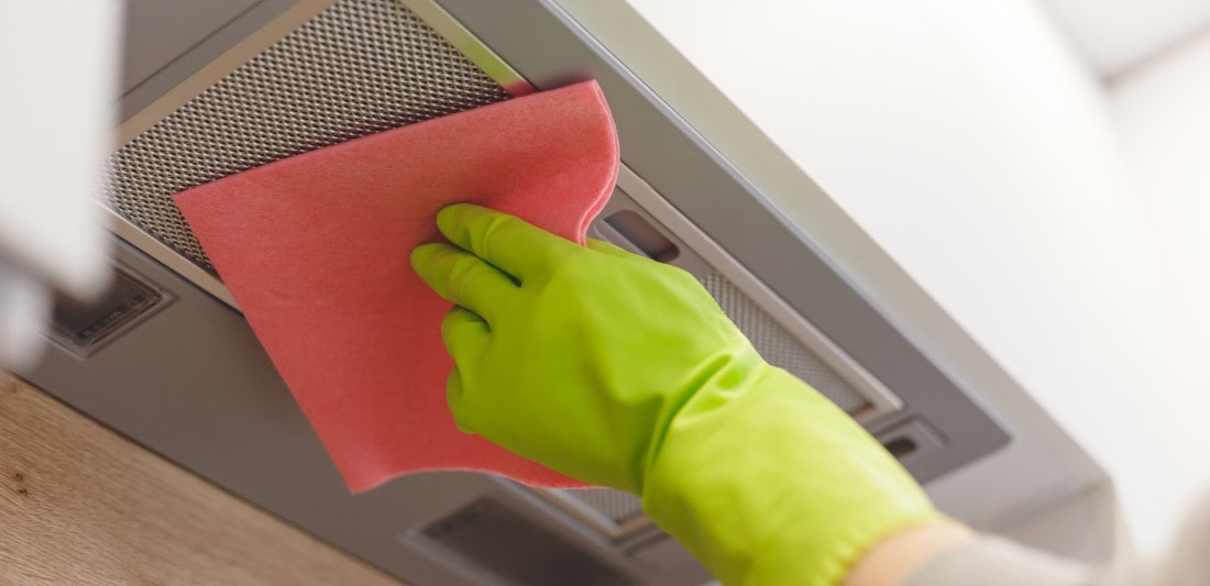 Homeowner in green marrigold gloves cleaning modern cooker hood.