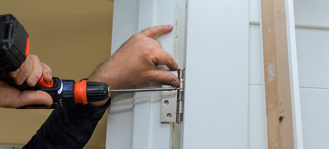 Worker fitting an internal door hinge using a drill driver.