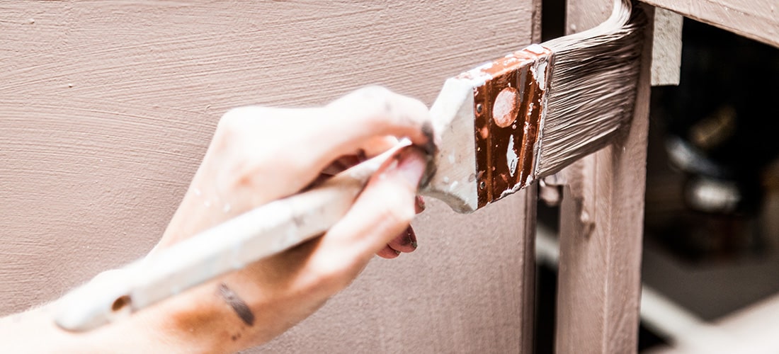 Close-up of homeowner painting kitchen cabinets with well used brush.