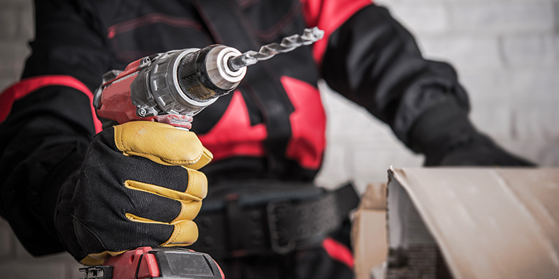 Worker in red and black jumpsuit holding a cordless power drill.