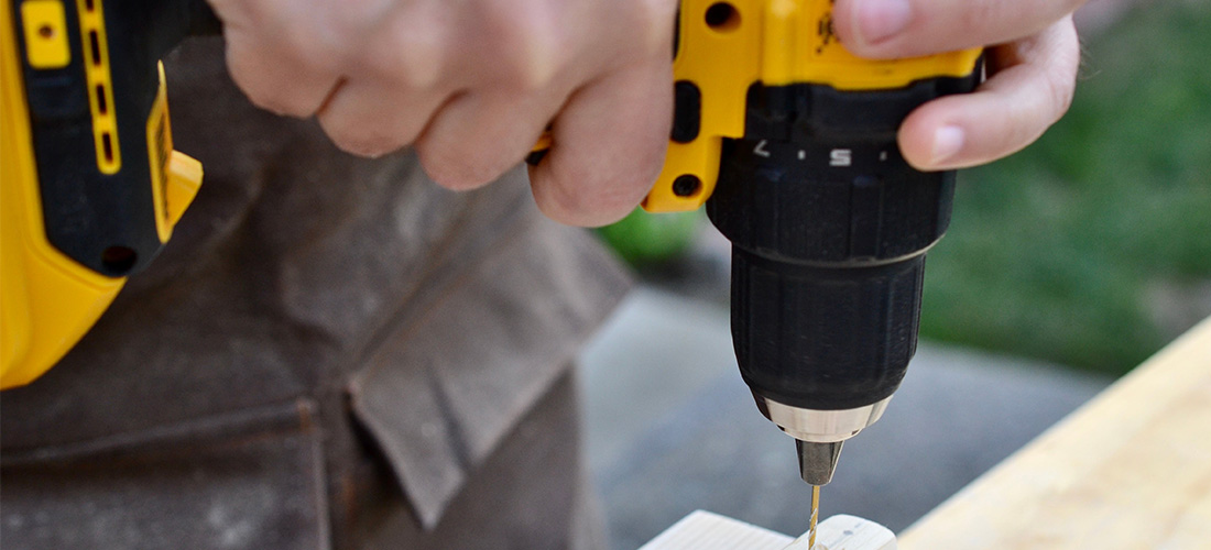 Worker drilling fixing hole into wooden board with a drill driver.