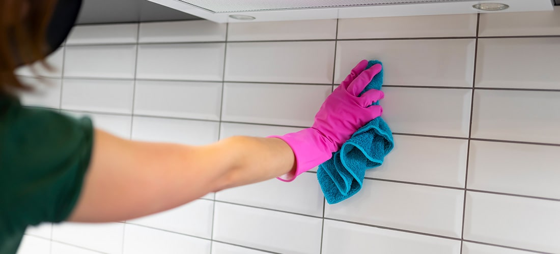 homeowner in pink marigold gloves cleaning kitchen tiles.