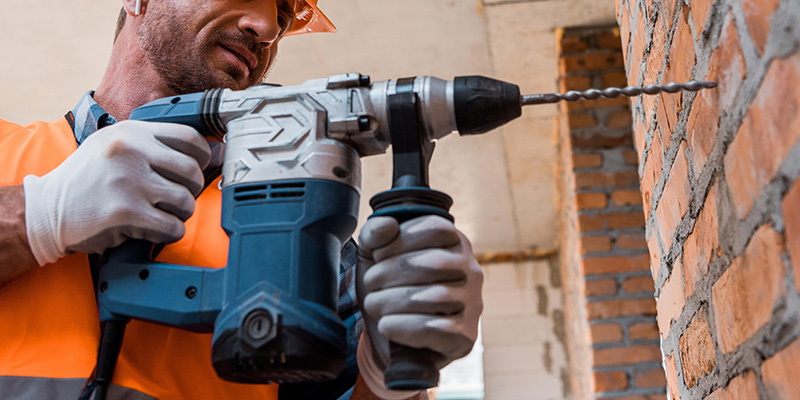 Builder in high-vis using a SDS drill to make fixing hole in brick wall.