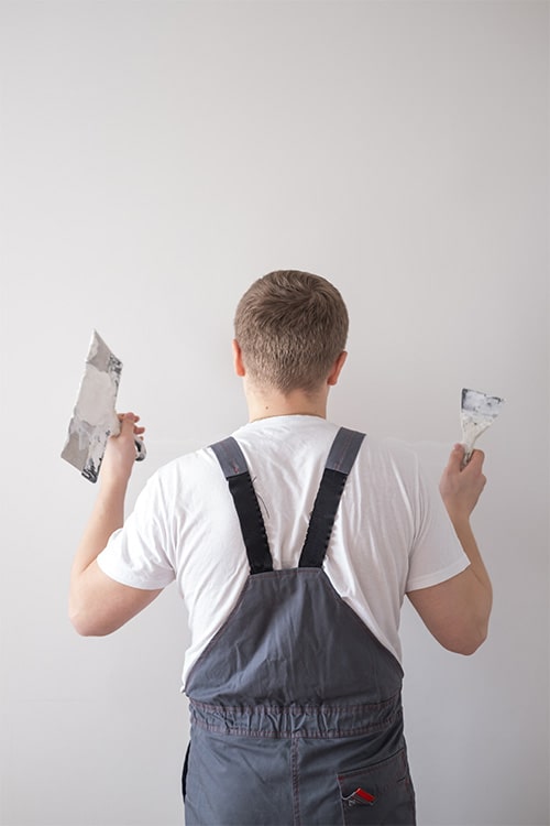 Worker in overalls repairing a wall with plastering tools.