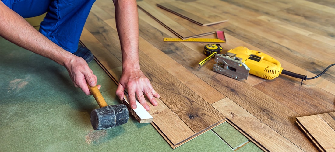 Worker hammering laminate flooring into place.