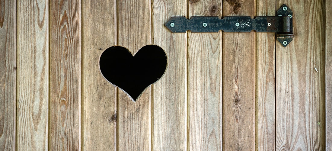 Black gate hinge on wooden door with heart-shaped peep hole.