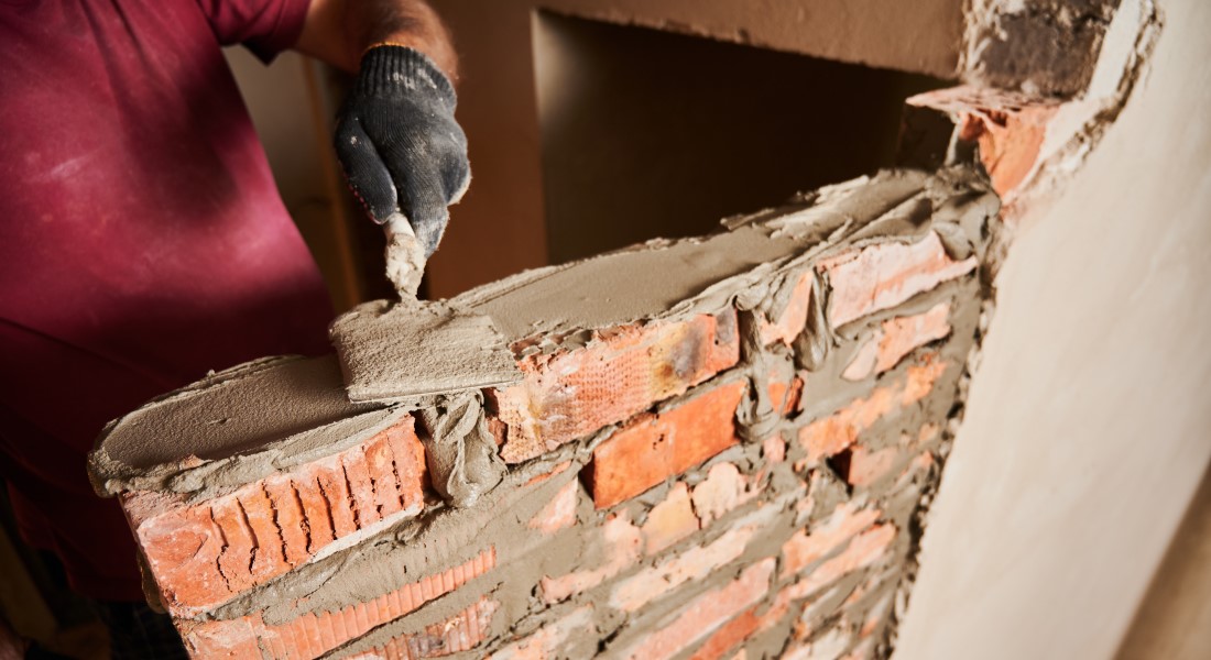 Workers spreading mortar on top course of brick wall.