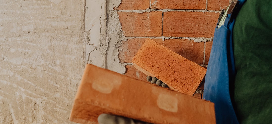 Builder holding two orange bricks in front of an under maintenance brick wall.