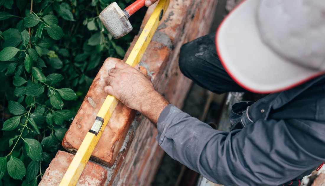 Proffesional builder checking that the brick wall he is  building is level with spirt level.