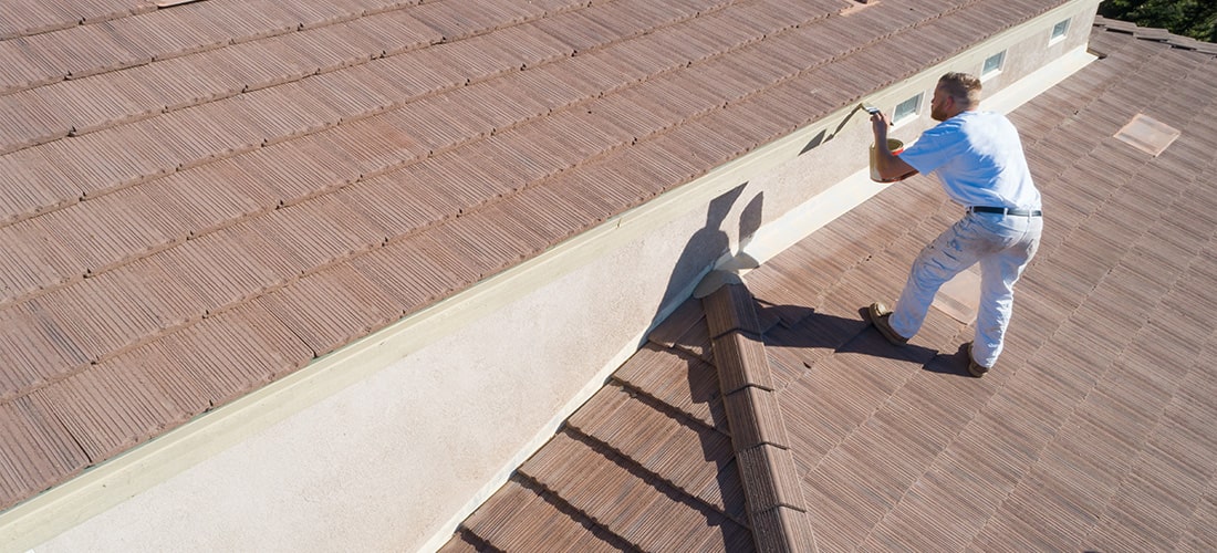 Proffesional painter standing on roof to paint high wall.