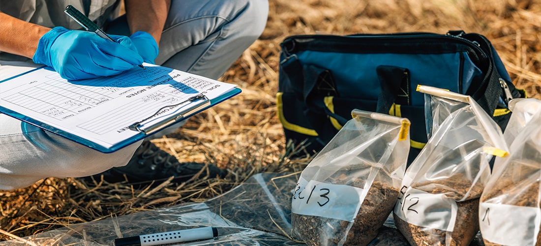 Scientist, holding clipboard, conducting soil test with bags of numbered soil.