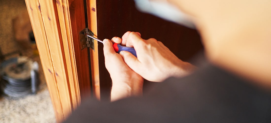 Homeowner using a screwdriver to fit a door hinge.