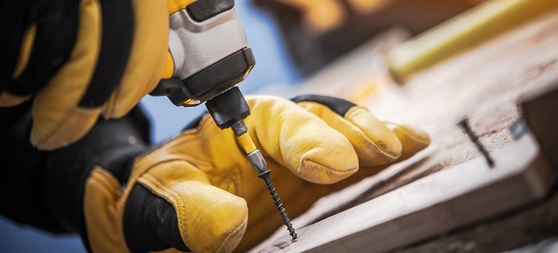 Worker with heavy-duty gloves driving in a screw.