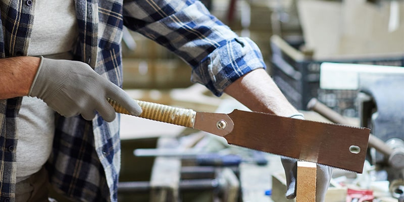 Wood worker cutting a wooden block with a pull saw.